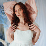 The Baby Antoinette Silk Hair Bow styled on a model with curled red hair and a white lace dress, emphasizing its dreamy and bold pink statement.