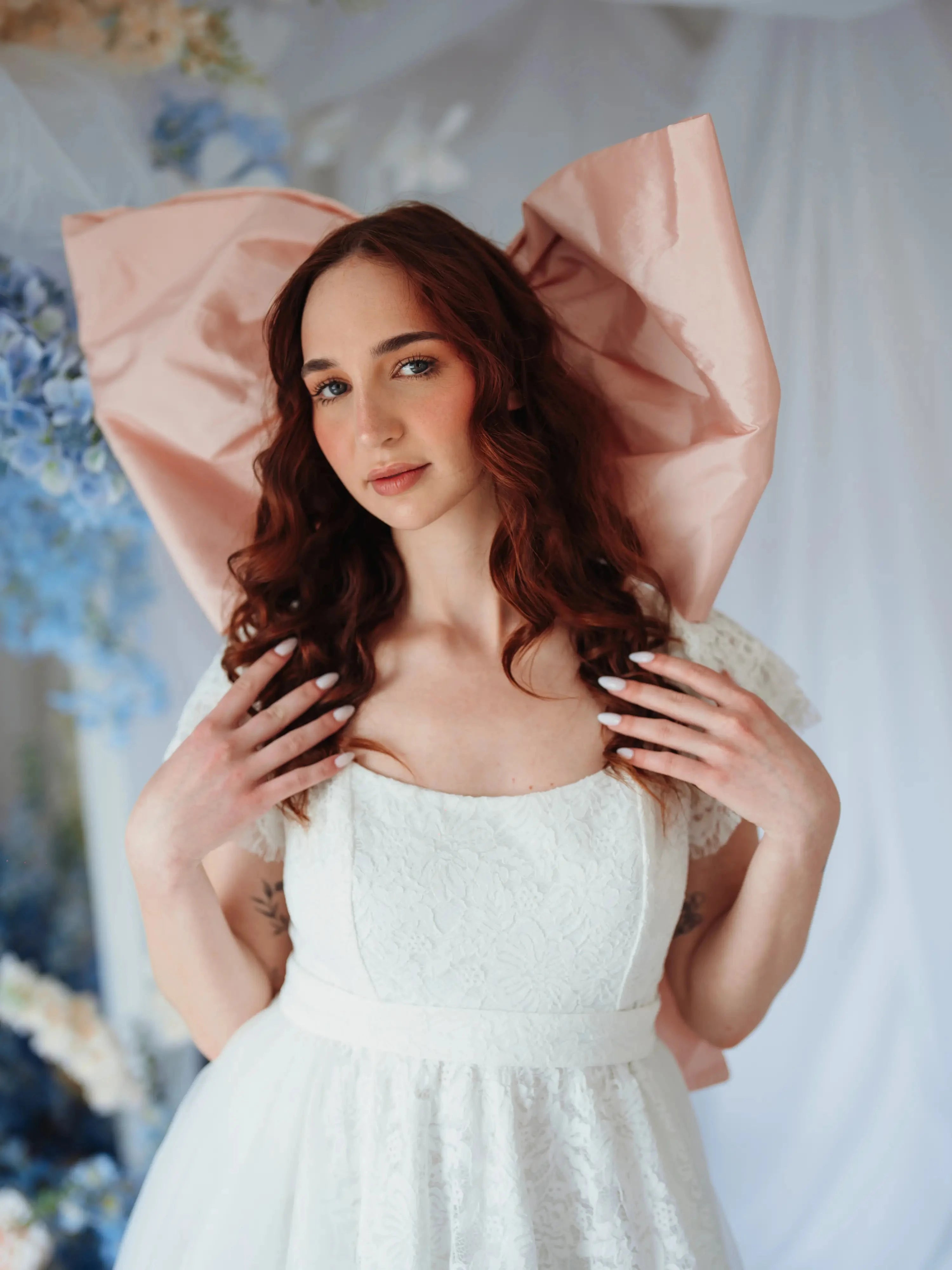 The Baby Antoinette Silk Hair Bow styled on a model with curled red hair and a white lace dress, emphasizing its dreamy and bold pink statement.