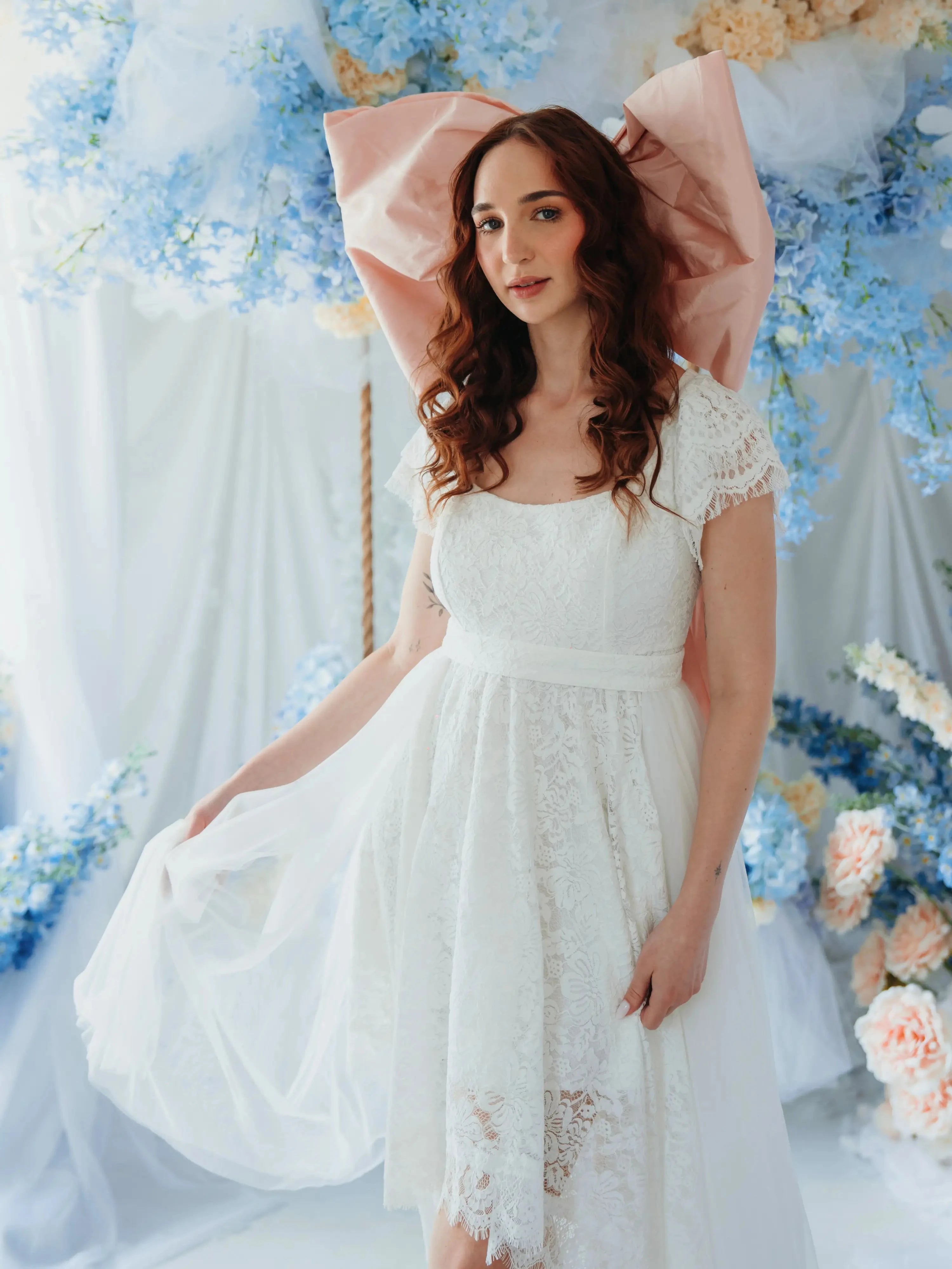 The Baby Antoinette Silk Hair Bow styled in a whimsical floral setting with a white lace dress, perfect for statement hair accessories.