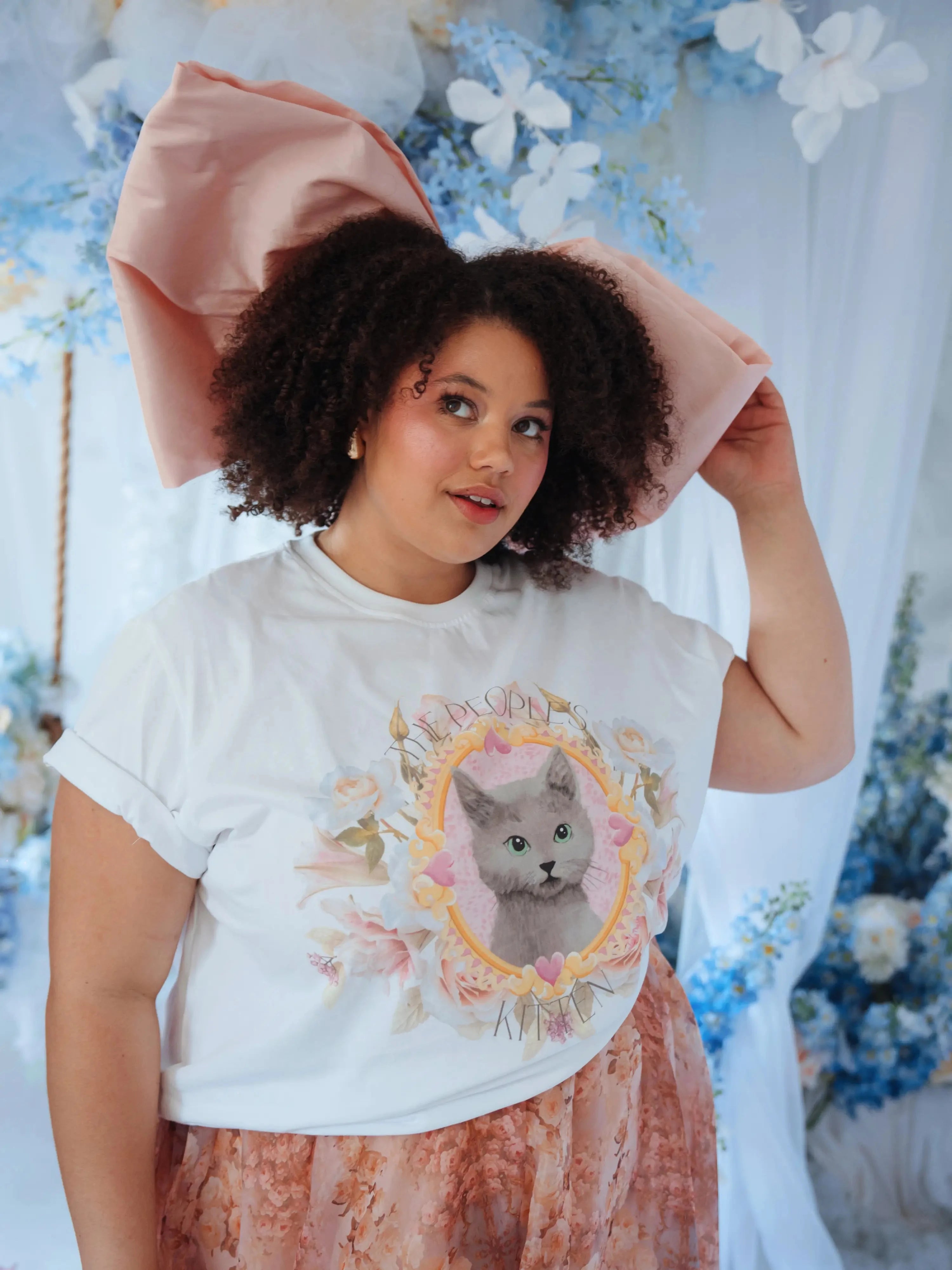 The Baby Antoinette Silk Hair Bow paired with a graphic cat tee and floral skirt, showcasing its dramatic oversized pink silhouette.