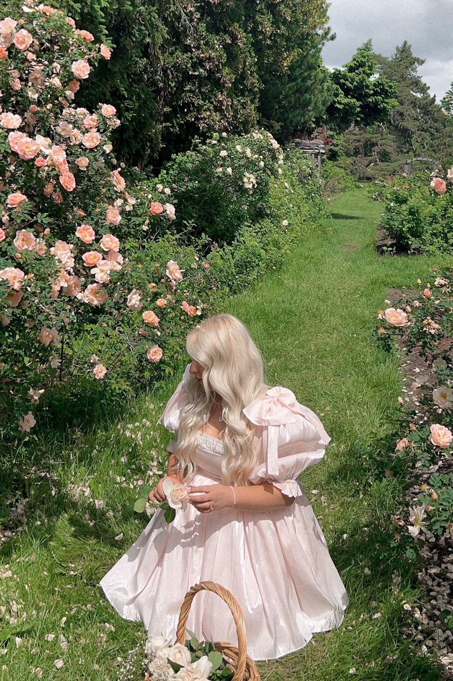 Girl in a pink dress surrounded by roses on a garden path wearing the Peach Da Vinci Puff Dress