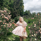 Woman in a pink puff dress standing elegantly among lush rose bushes, showcasing the Peach Da Vinci