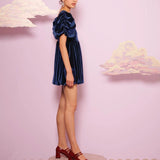 Woman in a navy blue velvet mini dress on a circular platform showcasing Spell Velvet Mini