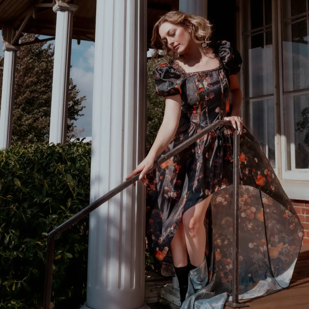 A woman in front of a house in a black taffeta corset gown with an autumn print.