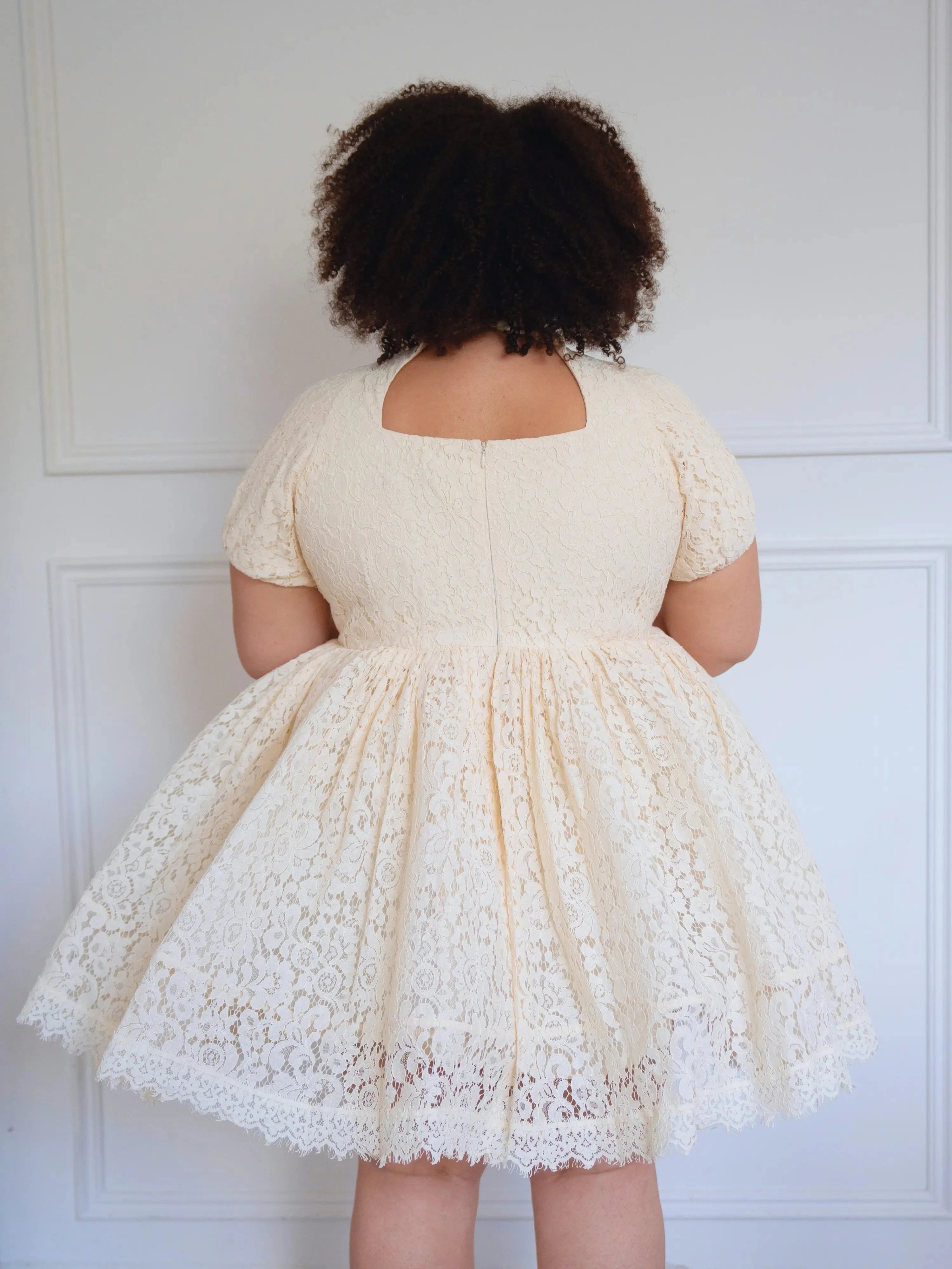 Back view of plus-size model in The Victorian Lace Tea Party Mini Dress showing full lace skirt and short puff sleeves.