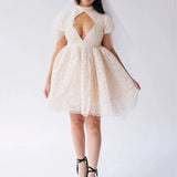 Woman wearing a white lace mini dress with a large diamond cutout on bust against a white background.