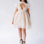 Woman wearing a white lace mini dress with a large diamond bust cutout against a white background