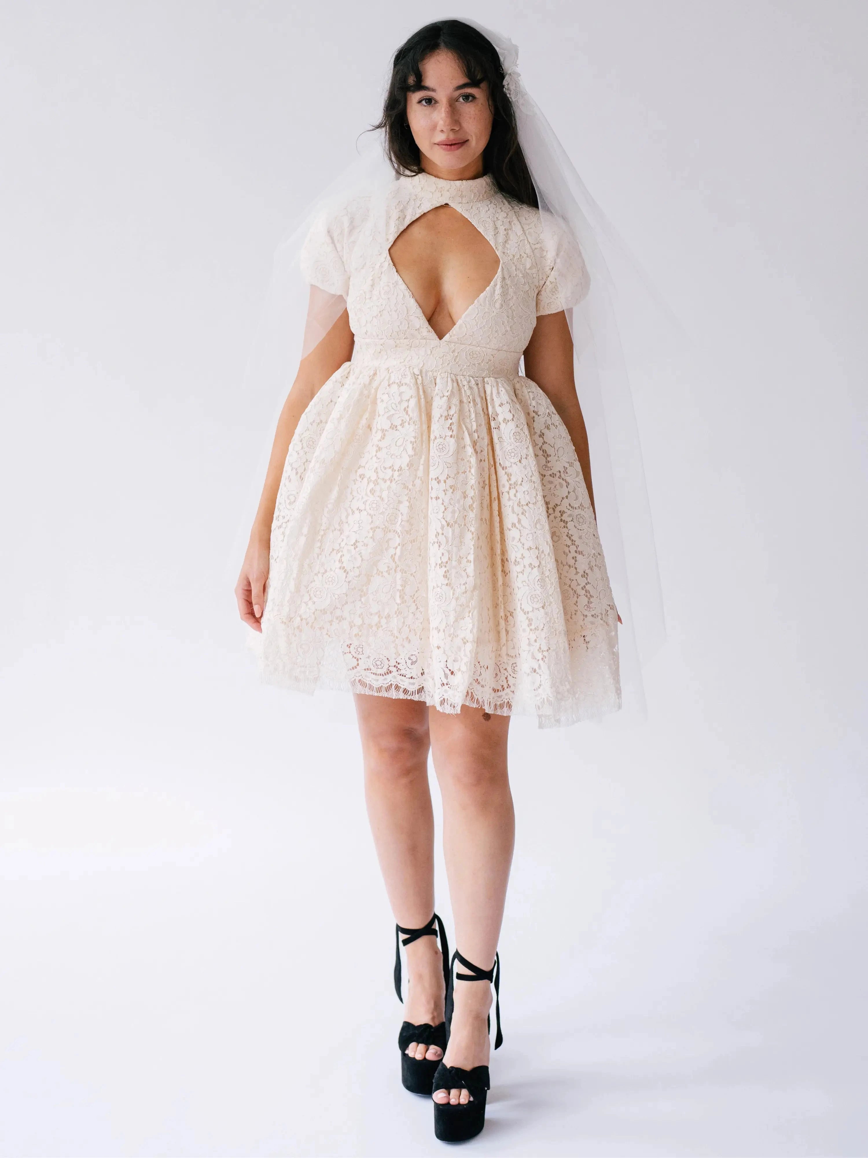 Woman wearing a white lace mini dress with a large diamond bust cutout against a white background
