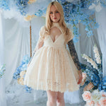 The Victorian Lace Tea Party Mini Dress in off white lace with puff sleeves on a model and styled in a floral setting.