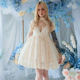 The Victorian Lace Tea Party Mini Dress in off white lace with puff sleeves on a model and styled in a floral setting.