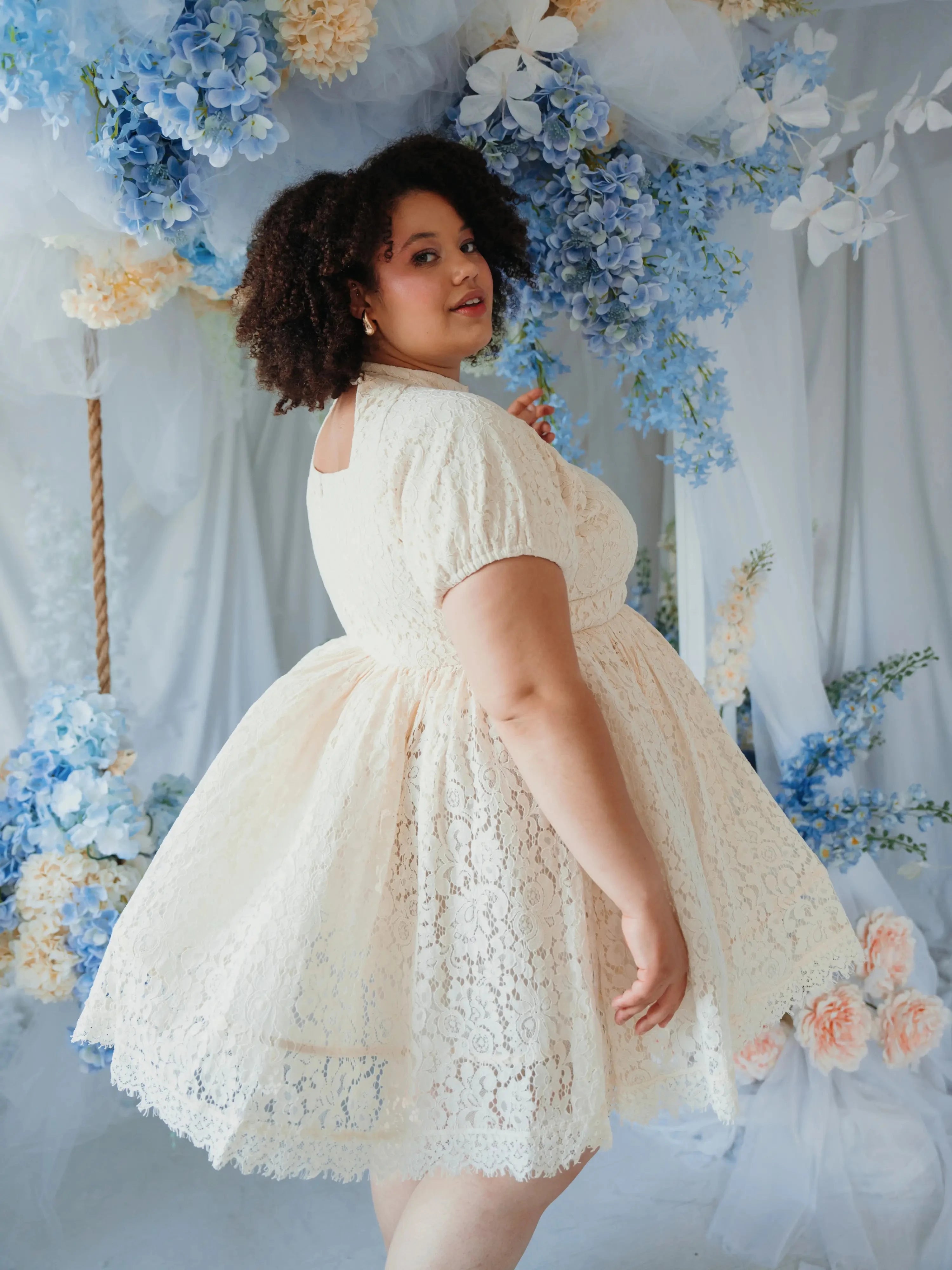 Back view of plus-size model twirling in The Victorian Lace Tea Party Mini Dress, highlighting lace detail and full skirt.