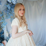 Side view of a woman wearing The Victorian Lace Tea Party Mini Dress showing lace texture and puff sleeves, styled in a romantic floral backdrop.