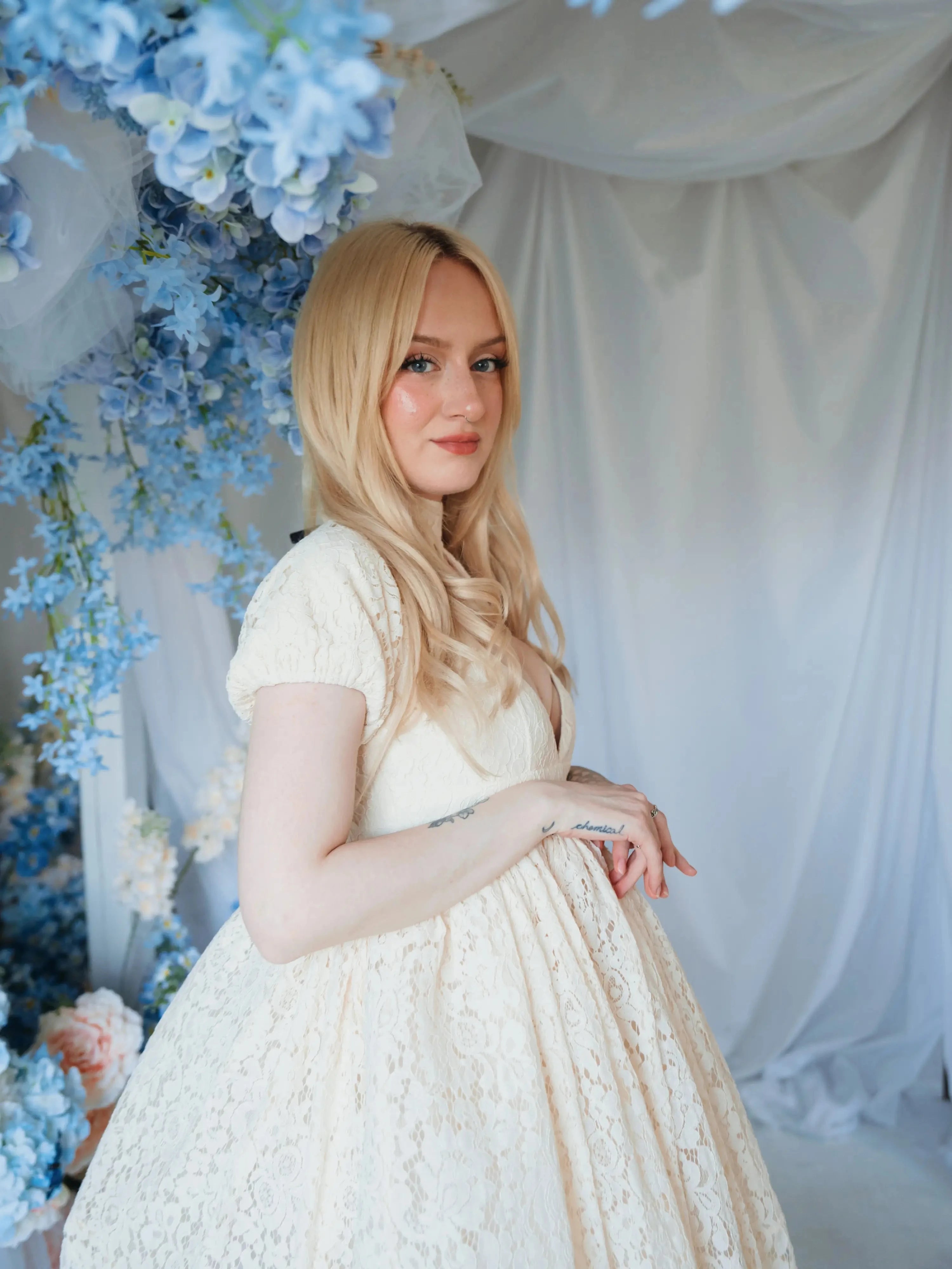 Side view of a woman wearing The Victorian Lace Tea Party Mini Dress showing lace texture and puff sleeves, styled in a romantic floral backdrop.