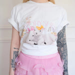 Front view of The Little Lamb Tee tucked into a pink layered lace skirt, featuring charming lambs and floral artwork for a dreamy look.