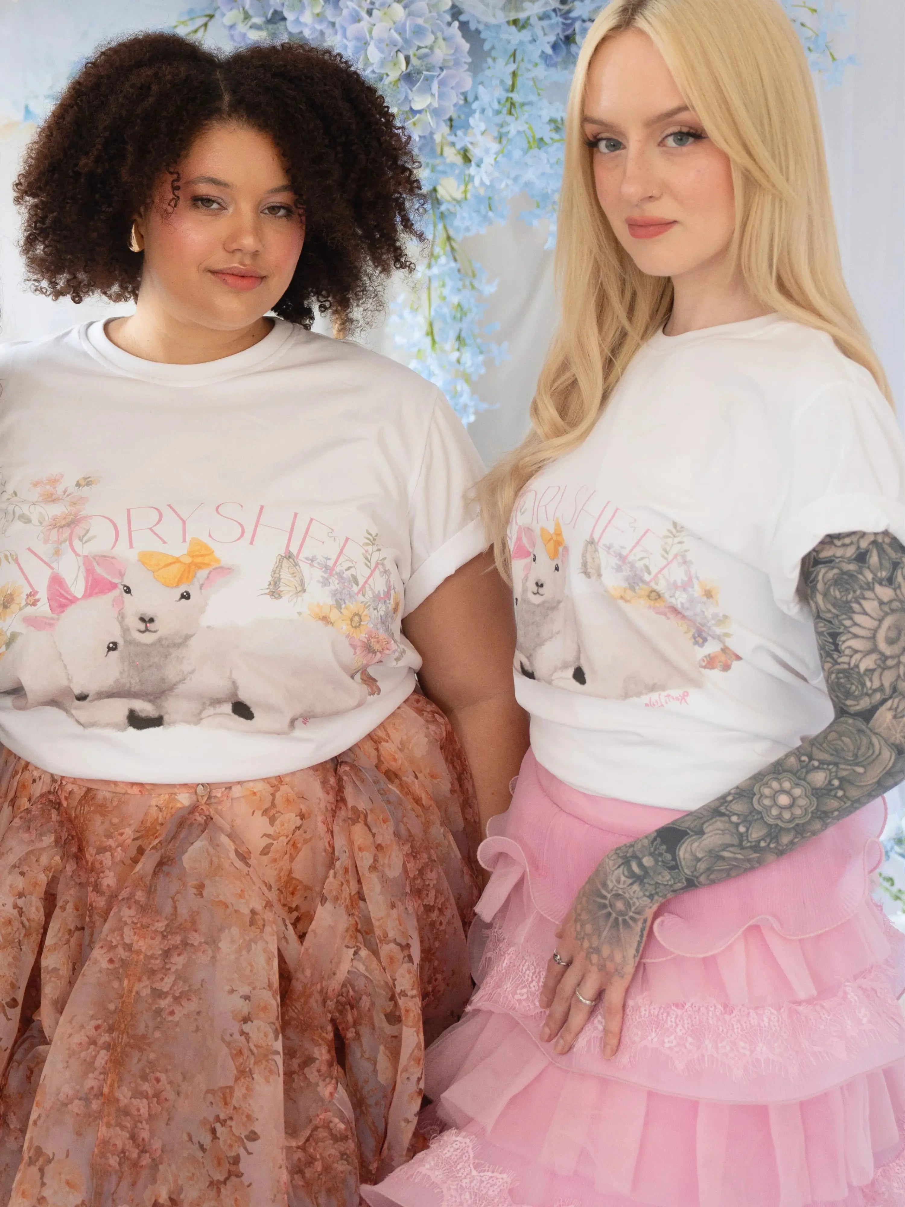 The Little Lamb Tee styled with pastel skirts, featuring whimsical lamb and floral artwork by Kaeti MacNeil. Cottagecore fashion for spring looks.
