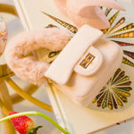 The Petit Agneau Tiny Purse in ivory with faux fur handle and gold clasp, styled on a decorative book for chic micro handbag appeal.