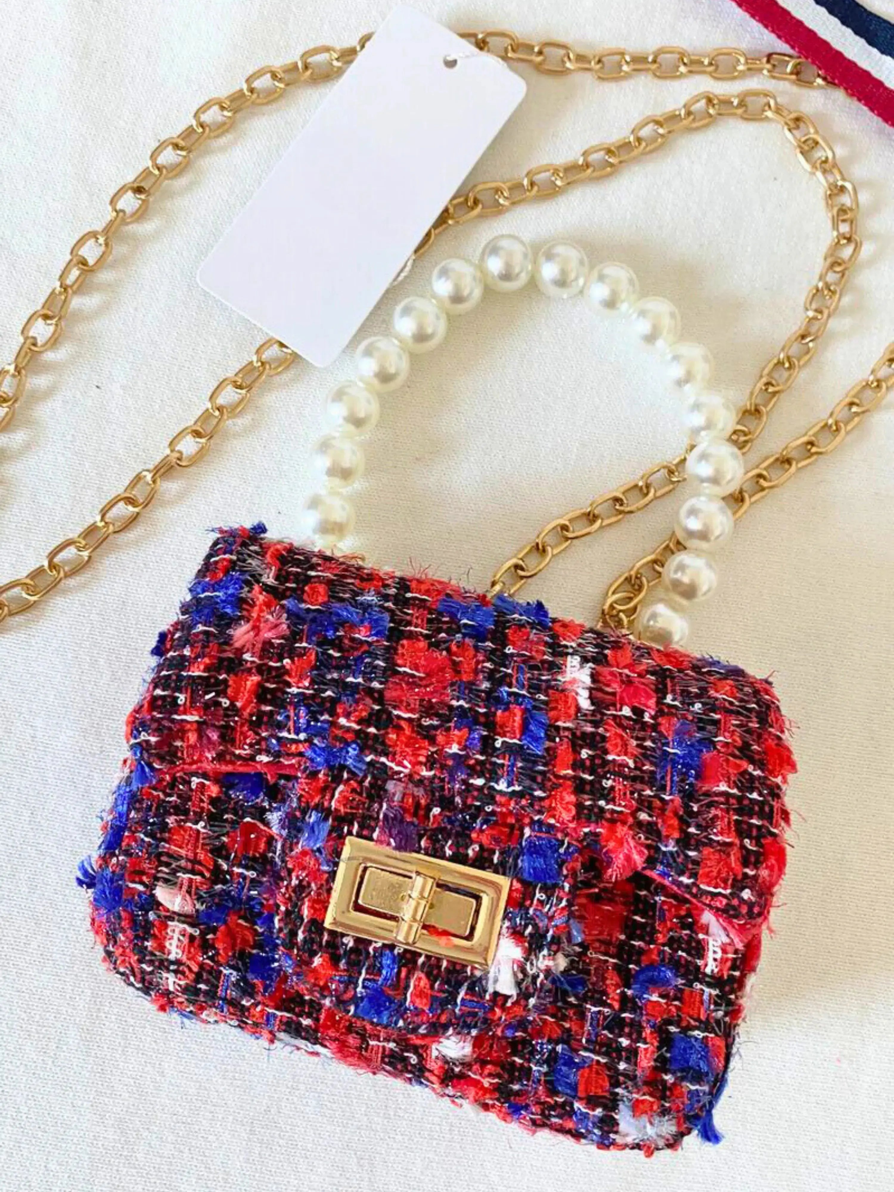 The Little Lady Tweed Mini Purse in red, blue, and black tweed with pearl handle and gold chain. Micro handbag ideal for chic, versatile styling.
