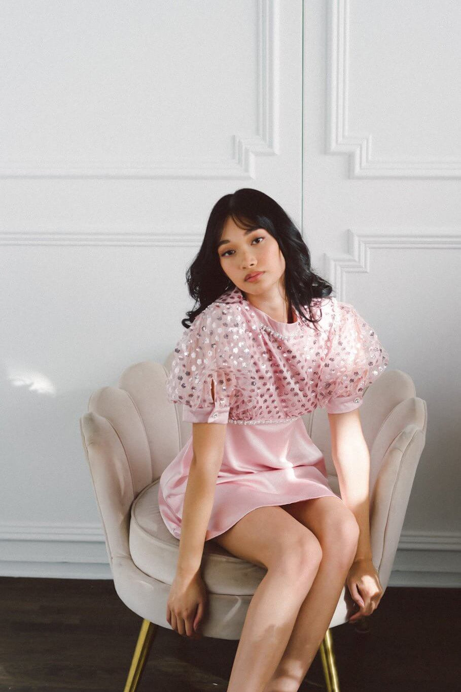 Woman in a pink Twizzle Embellished Mini Dress sitting in a cream armchair