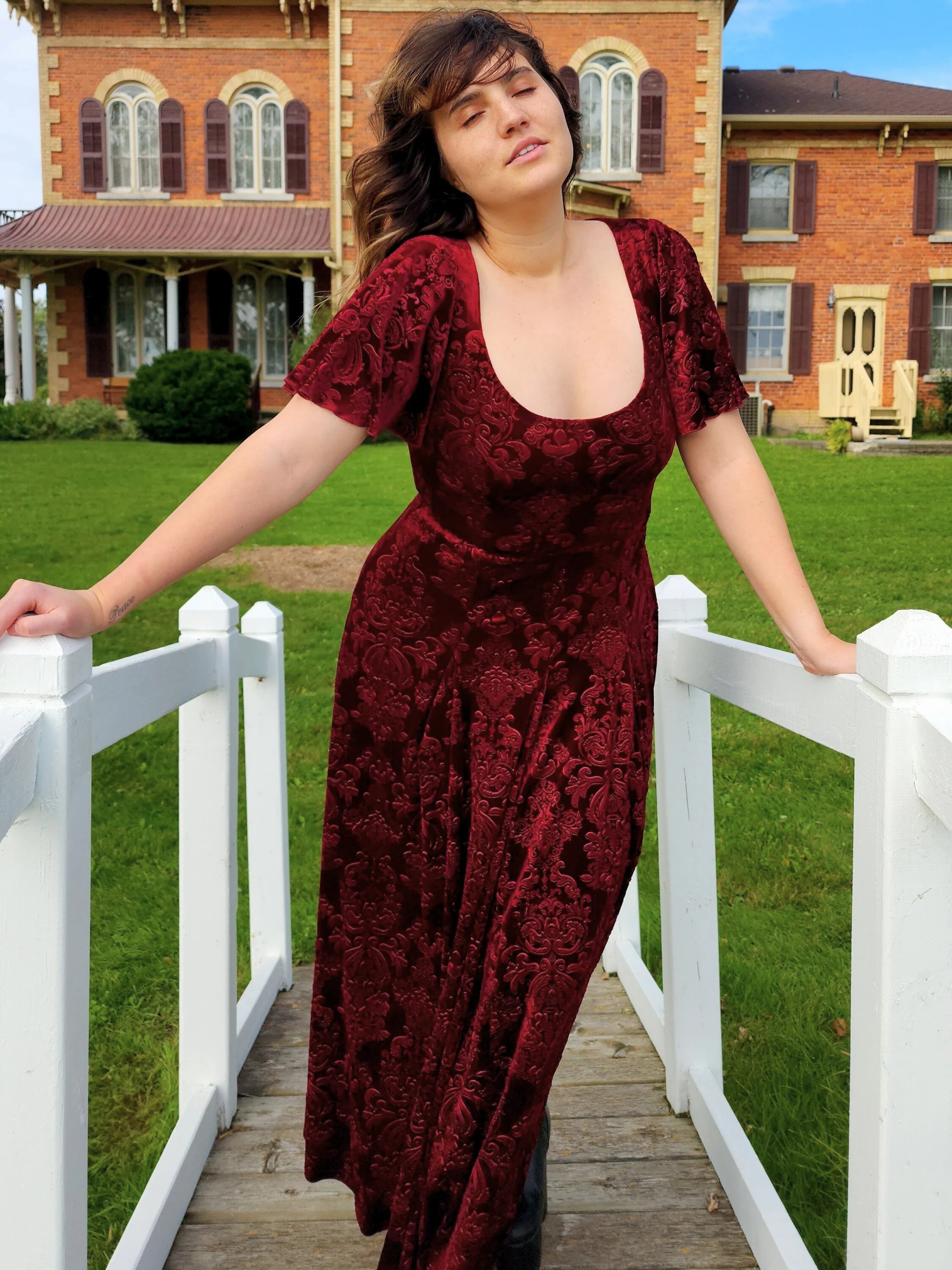 Woman in a long burgundy velvet dress on a white wooden bridge showcasing Velvet Viola Dress