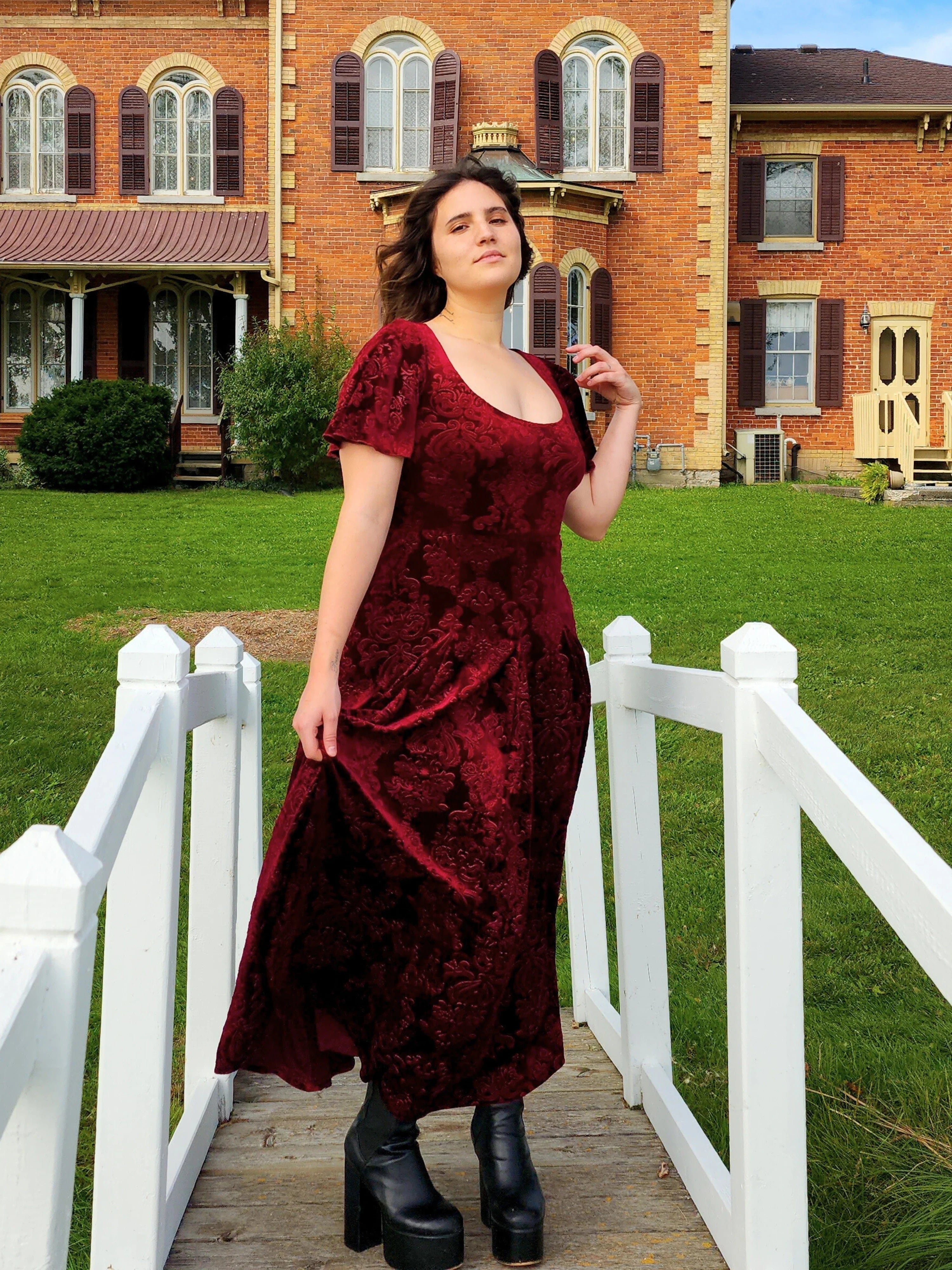 Woman in a long burgundy velvet dress on a white wooden bridge showcasing the Velvet Viola Dress