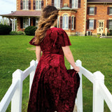 Woman in a flowing red Velvet Viola Dress walking on a white bridge