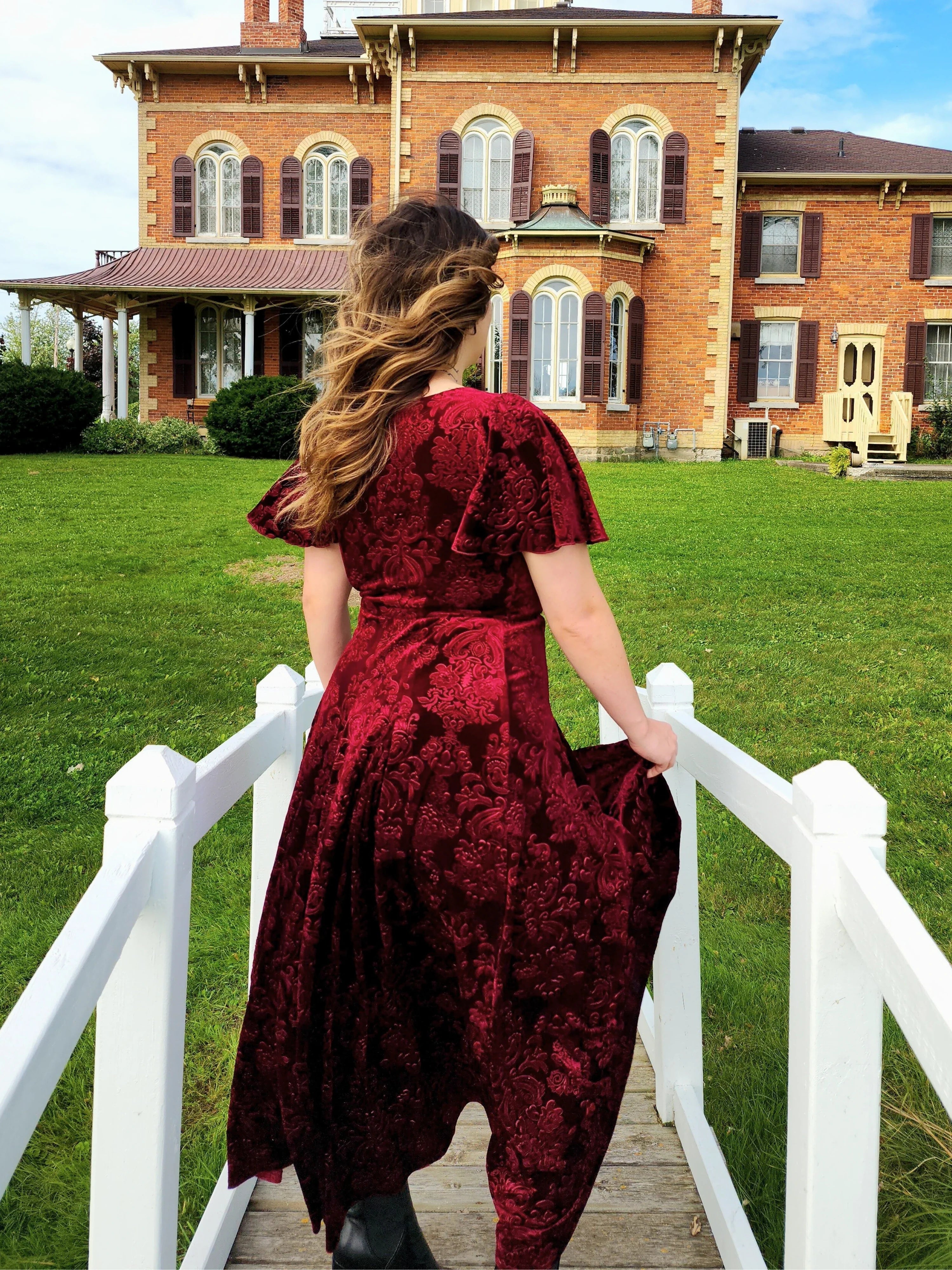 Woman in a flowing red Velvet Viola Dress walking on a white bridge