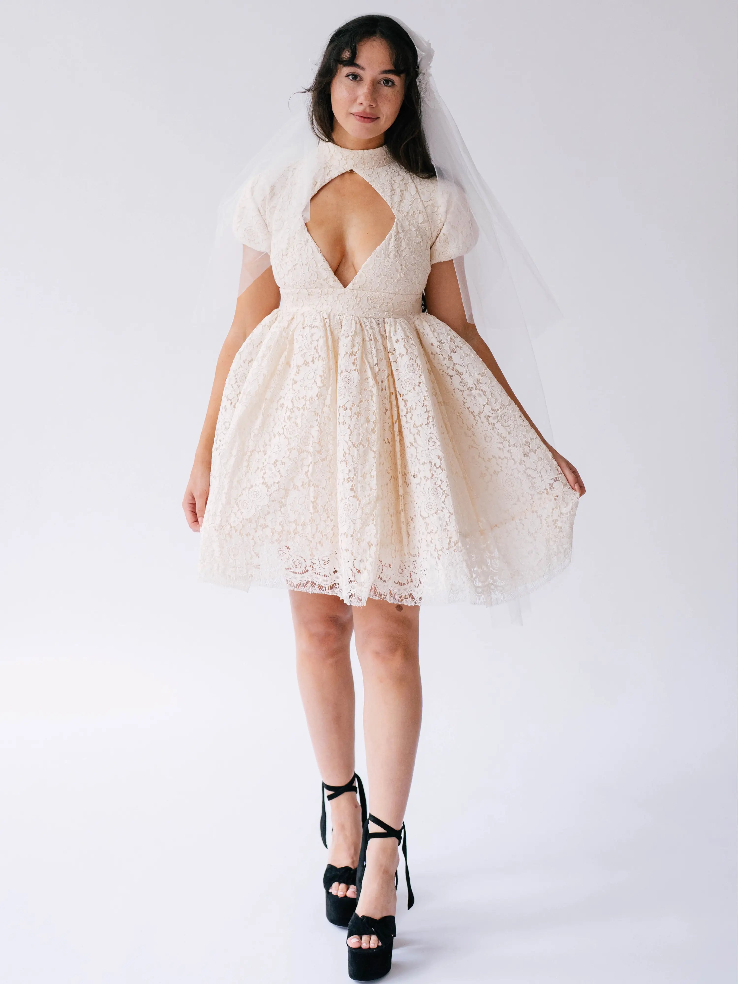 White lace mini dress with a keyhole neckline and short puffy sleeves paired with black platform heels.