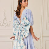 Woman in light blue dress featuring a large floral grand bow sash on the back