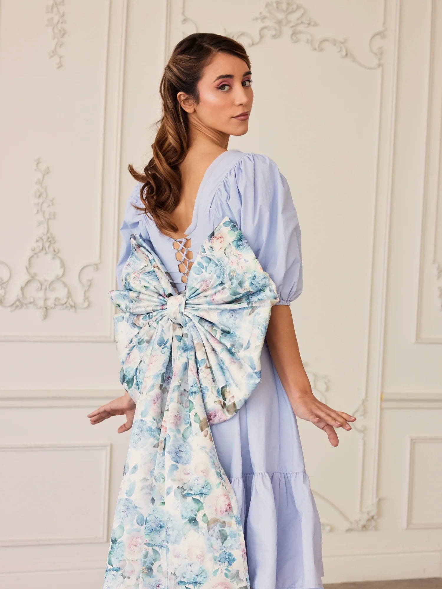 Woman in light blue dress featuring a large floral grand bow sash on the back