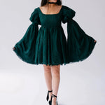 A woman wearing a green bell sleeve dress on a white background.